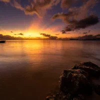 Sunset over a calm shoreline, with rocks in the foreground