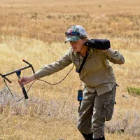 A researcher walking through a dry grass field with tracking equipment